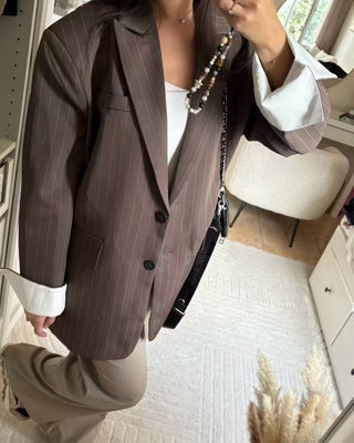 Blazer oversize marron à fines rayures blanches, coupe droite structurée avec épaules marquées, porté avec un jean noir et des baskets montantes.