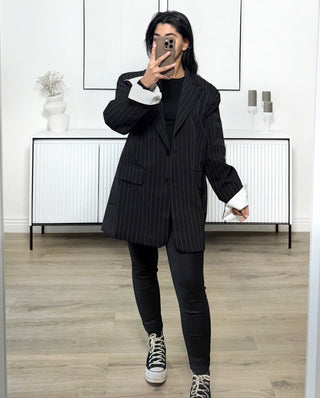 Blazer oversize noir à fines rayures blanches, coupe droite structurée avec épaules marquées, porté avec un jean noir et des baskets montantes.