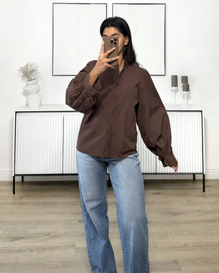 Chemise oversize marron à manches ballon, col classique et poignets boutonnés, portée avec un jean bleu.