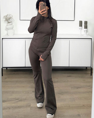 Ensemble de sport marron pour femme avec veste zippée ajustée et pantalon évasé en tissu stretch.