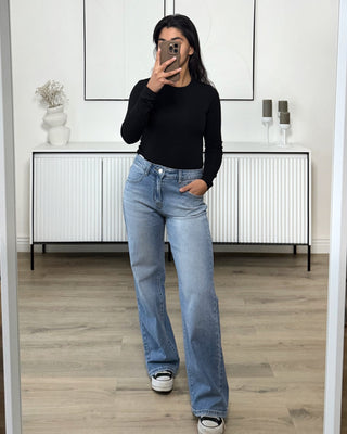 Jean en denim bleu clair à taille haute et coupe droite, porté par une femme avec un haut noir à manches longues, vue de face.