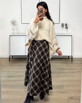 Jupe longue fluide à carreaux dans des tons noirs et beiges, coupe évasée élégante, portée avec un pull beige et des bottines, style chic et intemporel.