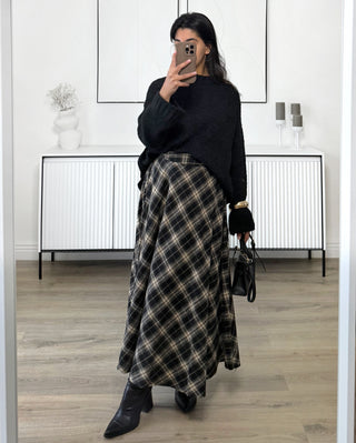 Jupe longue fluide à carreaux dans des tons noirs et beiges, coupe évasée élégante, portée avec un pull noir et des bottines, style chic et intemporel.
